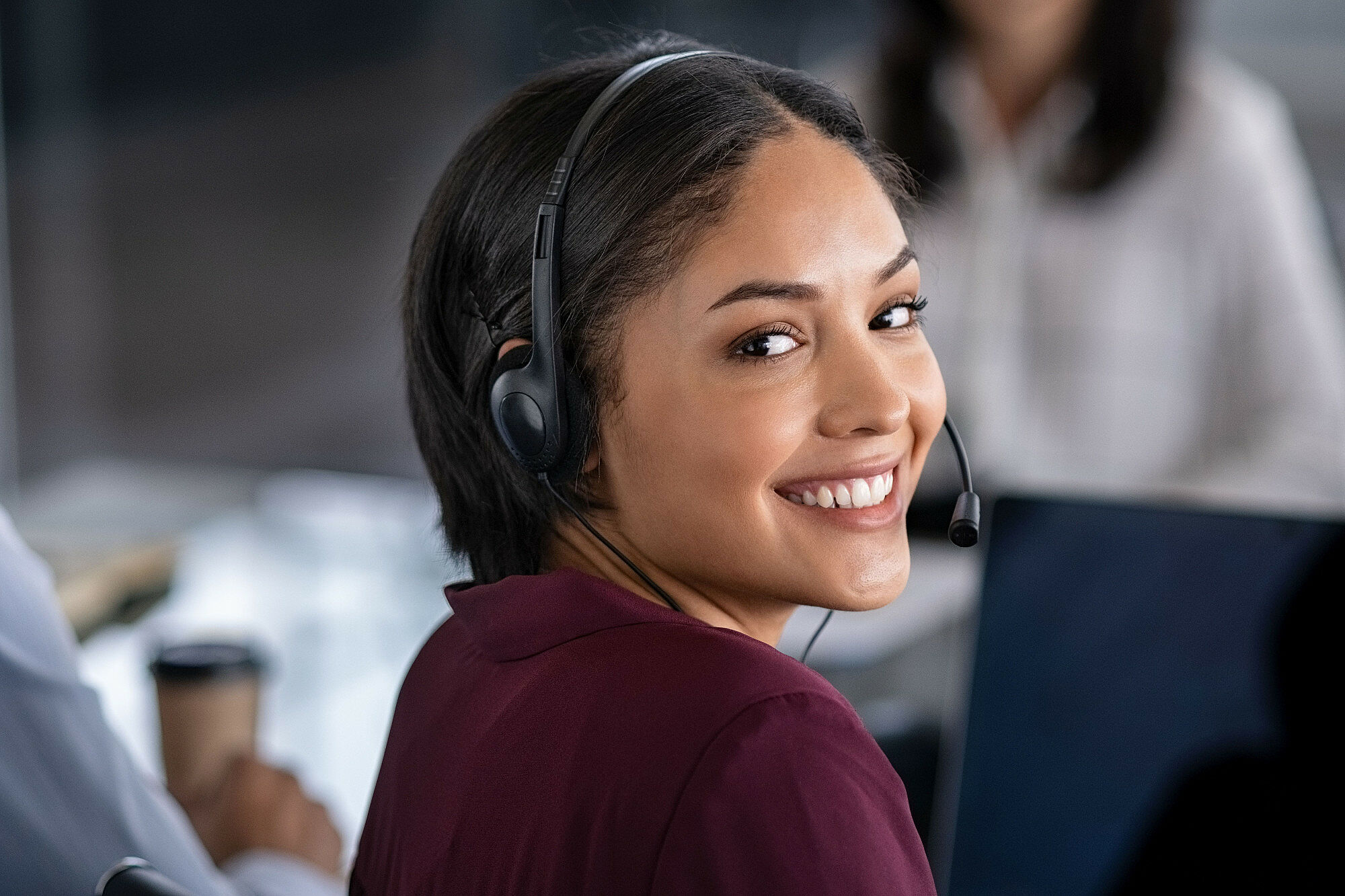 Portrait of smiling young businesswoman wearing headset in office. Portrait of a customer service agent looking at camera. Happy telephone operator latin girl with headset working at computer.
